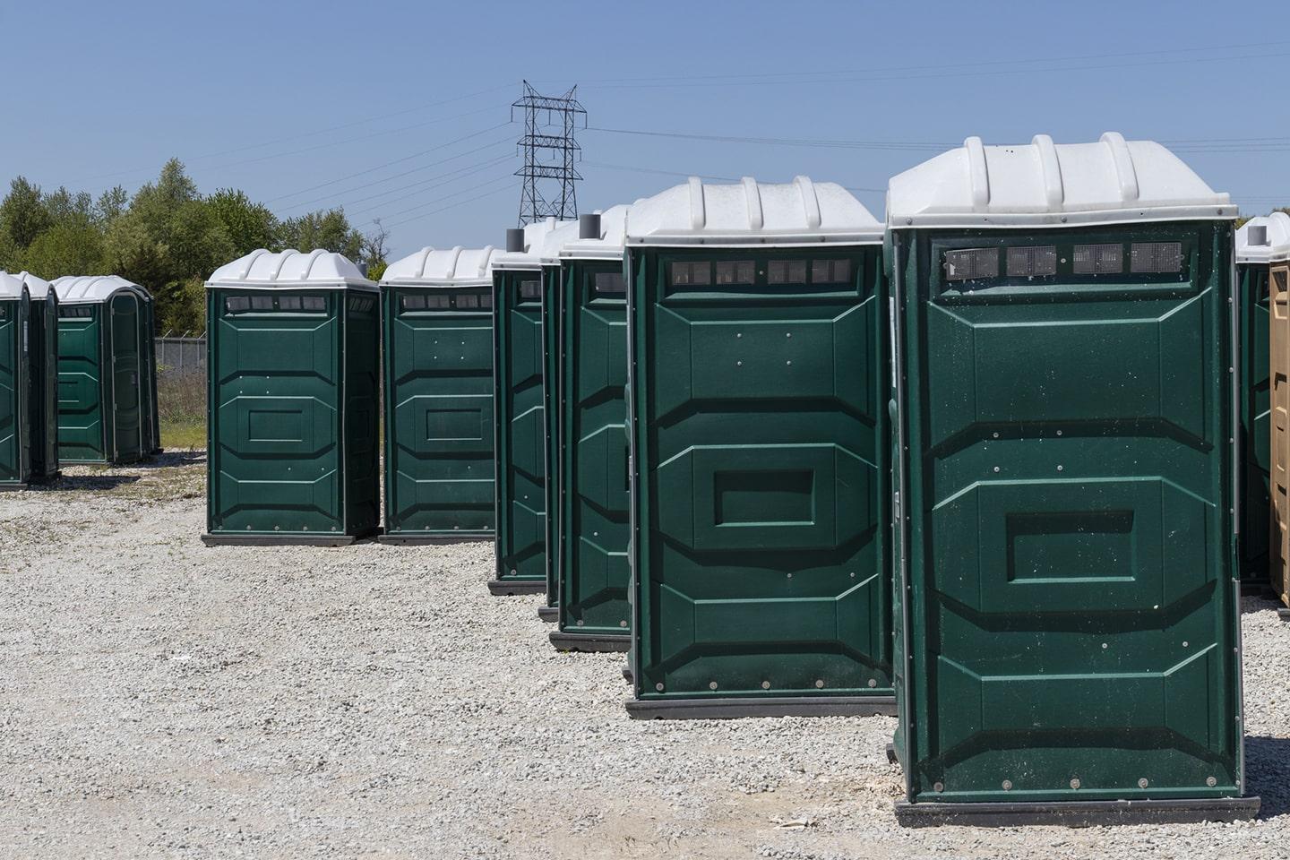 A row of clean, well-maintained green portable toilets staged for delivery
